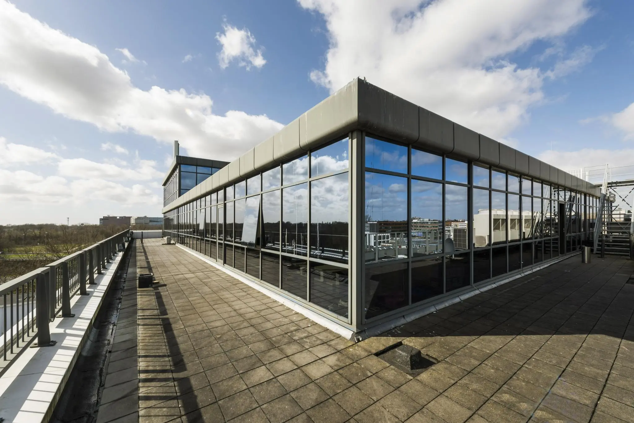 Dakterras met glazen gevel van een modern kantoorgebouw aan de Anthony Fokkerweg onder een blauwe lucht met wolken.